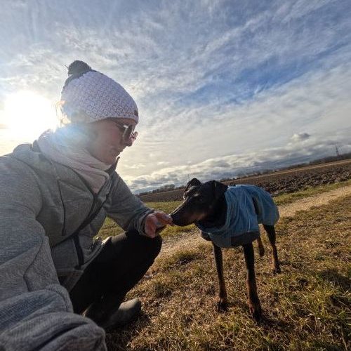 Eine Person mit lila Kopfbedeckung und ein Hund posieren zusammen.